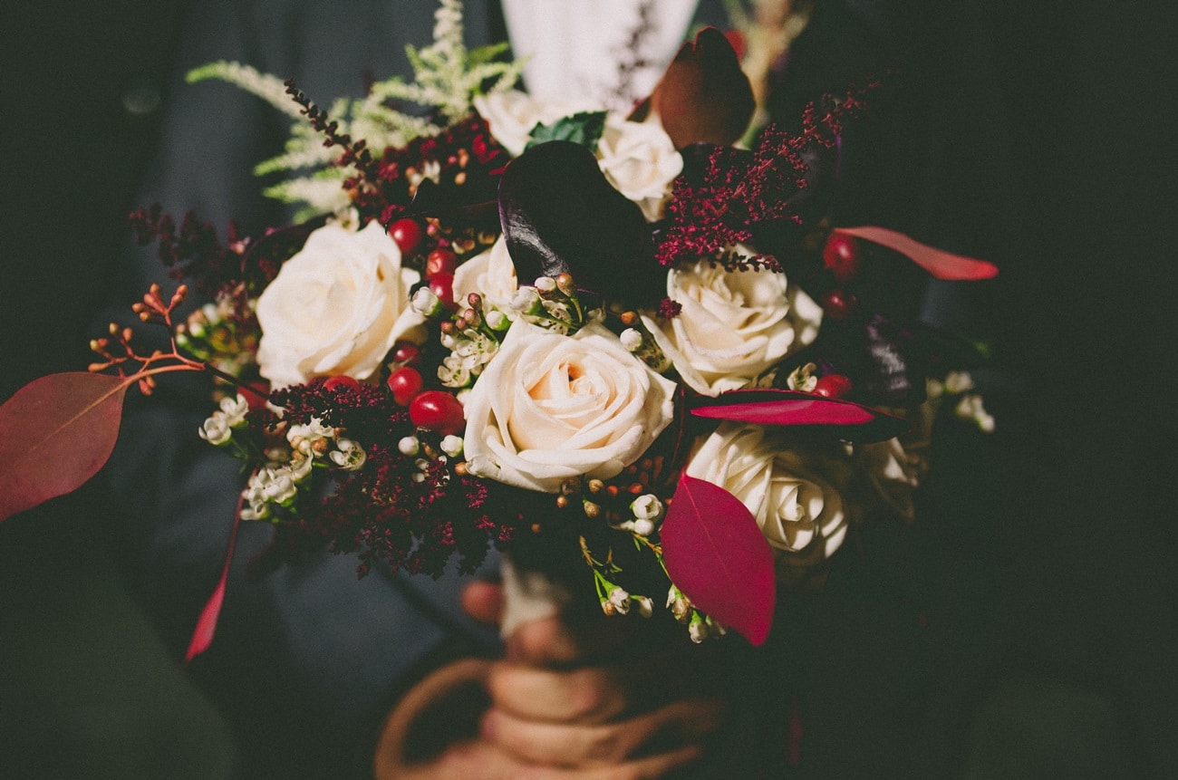Νυφική ανθοδέσμη με λευκά τριαντάφυλλα και κόκκινες λεπτομέρειες