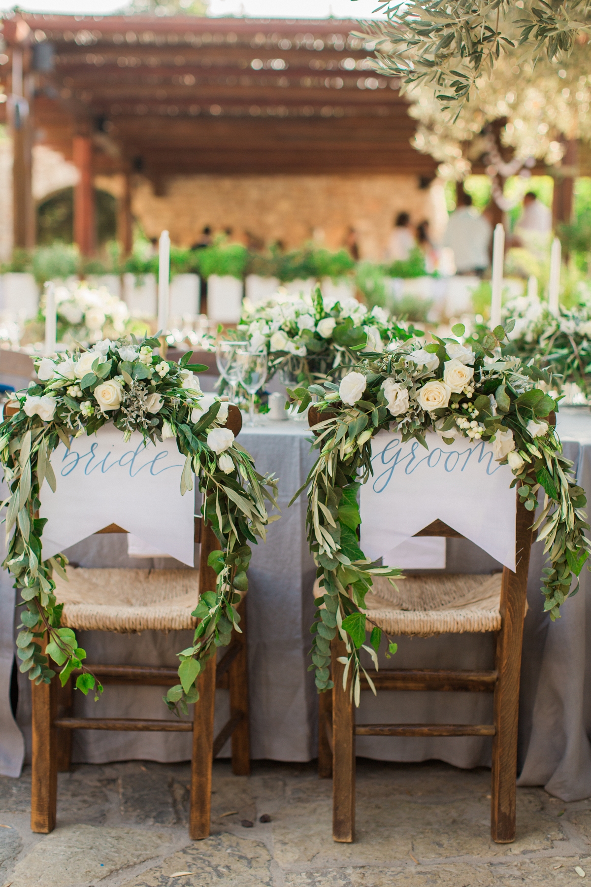 Καρέκλες νύφης και γαμπρού με λευκά τριαντάφυλλα, κισσό και φύλλα ελιάς